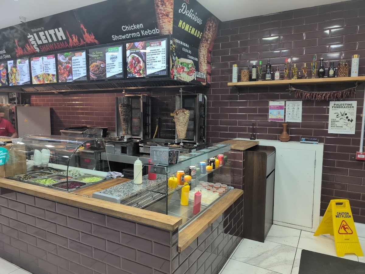 The counter: backlit menu boards for sides, falafel, pizzas, grill, platters and wraps under a banner reading 'Welcome to Leith Shawarma', with 'Delicious, Homemade — Shawarma, Kebabs, Tandoori' on the corner and maroon tiles behind.