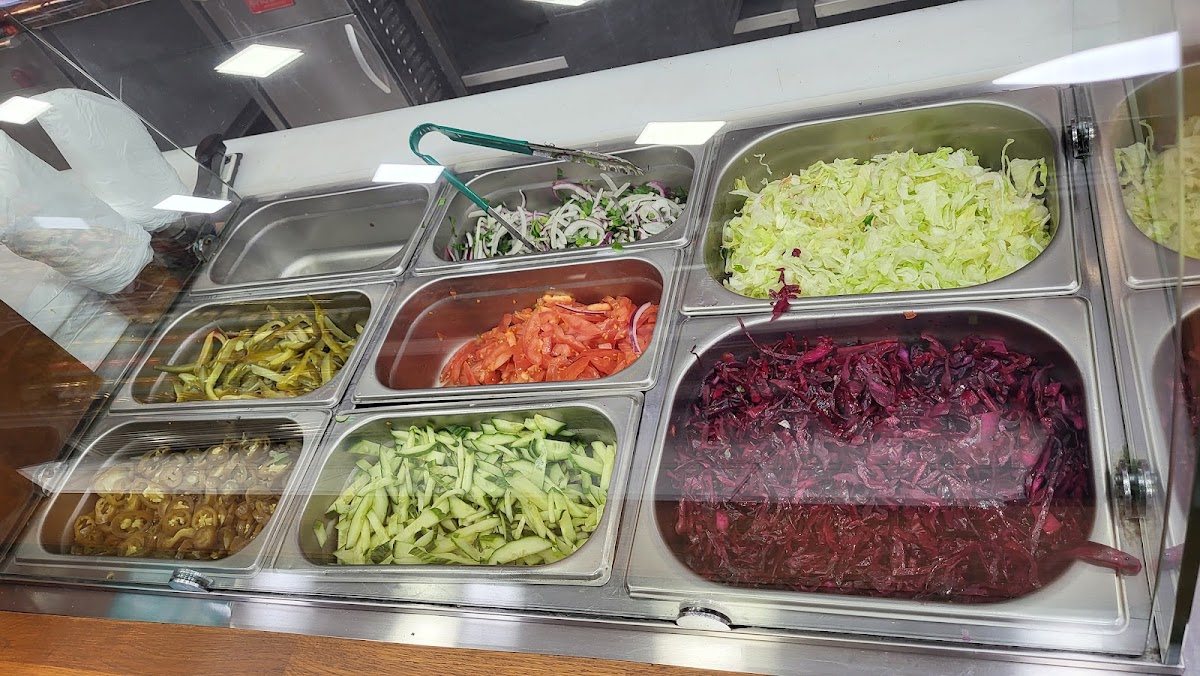 The salad bar under glass: shredded lettuce, red cabbage, sliced onion, chopped tomato, cucumber, pickled chillies and pickles in steel trays.